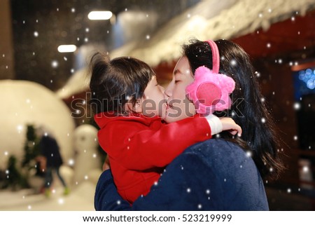 Adorable little girl kissing her mother in snow, Winter time.