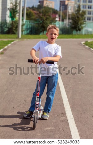 The boy on the scooter, standing on the street in the summer, on the roadway, traffic, pedestrian crossing, photography, open look at the camera warm summer day