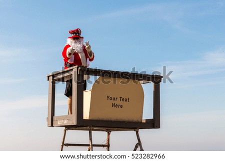 Santa Claus Isolated on old lifeguard tower in front of clear blue sky with a blank sign with room for you text