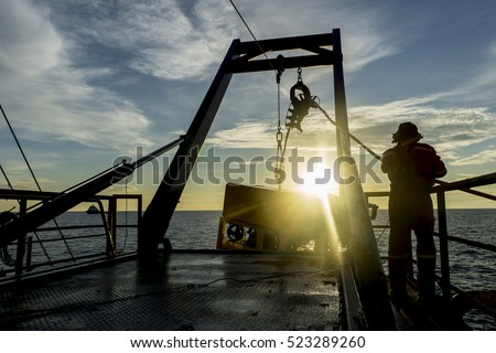 Silhouette of worker recovering robotics Remote Operated Vehicle (ROV) after entering sea surface during oil and gas pipeline inspection in the middle of South China Sea isolated on sunrise with glare Royalty-Free Stock Photo #523289260