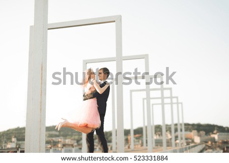Pretty sunny outdoor portrait of young stylish couple while kissing on the roof with city view