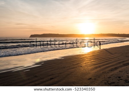 Golden light and silhouette of young boy alone on the beach in Coronado, California with Point Loma in the background.