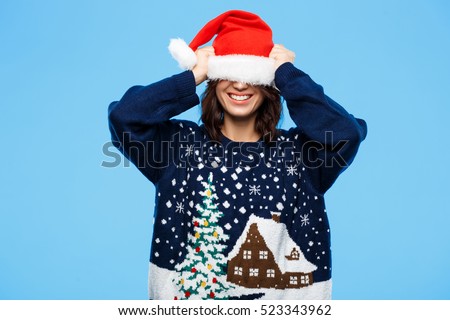 Young beautiful brunette girl in knited sweater and christmas hat smiling  over blue background.