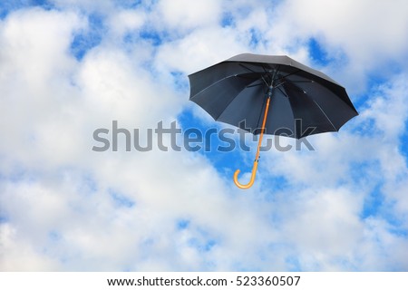 Black umbrella flies in sky against of pure white clouds.Mary Poppins Umbrella.Wind of change concept. Royalty-Free Stock Photo #523360507