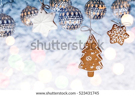 gingerbread christmas tree cookie hanging by twine over blurred silver background