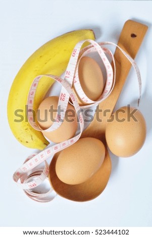Isolated picture of eggs, banana, wooden spoon and measuring tape. Concept idea what to eat for good shape and healthy.