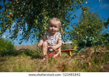 the little blonde girl plays in the garden with a basket of apples