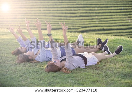 holidays and tourism, friendship concept - beautiful asian girls lay on green grass with two hands up mean cheer up sign.