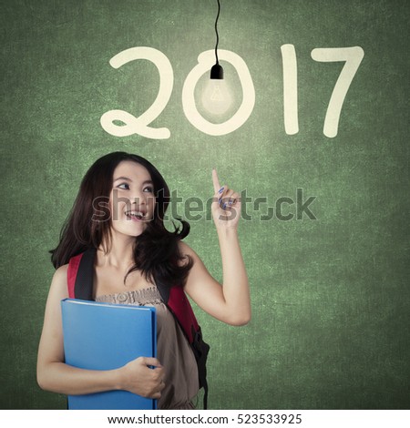 Image of beautiful woman student holding a folder with bright bulb and numbers 2017 on the chalkboard