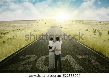 Picture of young happy family pointing bright sun light while standing on the road with numbers 2017