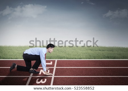 Picture of young Arabian businessman in ready position while kneeling in the line start on the track