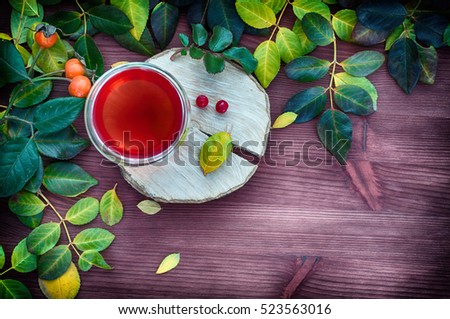 Tea in a transparent glass mug among the leaves on a brown wooden background