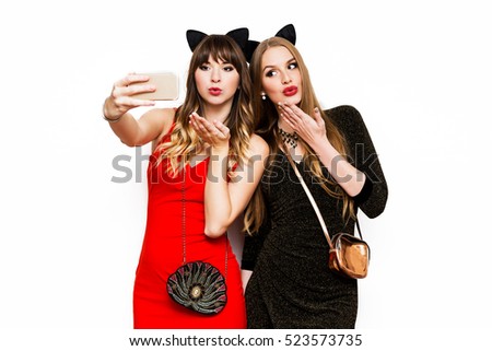 Two women having great time together, making self portrait , use carnival funny cat ears, wearing elegant evening dress. Friends celebrating new year or birthday party. Isolate white.