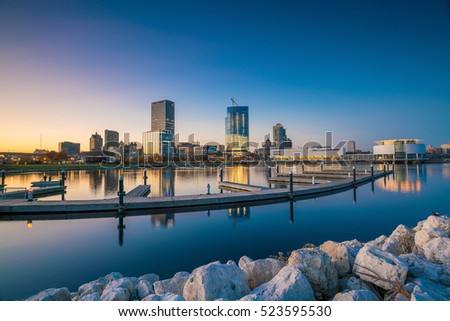 Milwaukee skyline at twilight with city reflection in lake Michigan and harbor pier.