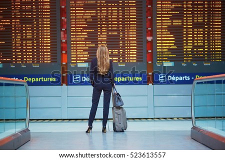 Young elegant business woman with hand luggage in international airport terminal, looking at information board, checking her flight. Cabin crew member with suitcase. Royalty-Free Stock Photo #523613557