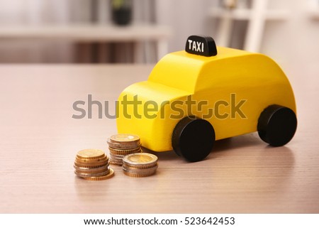Yellow toy taxi cab and coins on wooden table