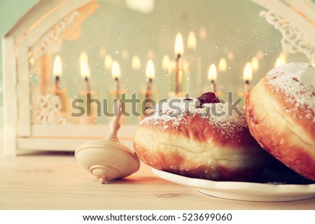 Selective focus image of jewish holiday Hanukkah with menorah (traditional Candelabra), donuts and wooden dreidel (spinning top)

