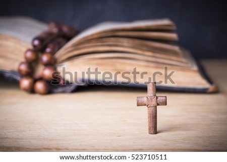 Brown cross and rosary on the Bible on a wooden background. Holy book.
