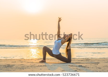 Young healthy Yoga woman workout yoga pose on the beach at sunrise, benefits of natural environments for physical, spiritual, healthy, relaxing concept.  Royalty-Free Stock Photo #523736671