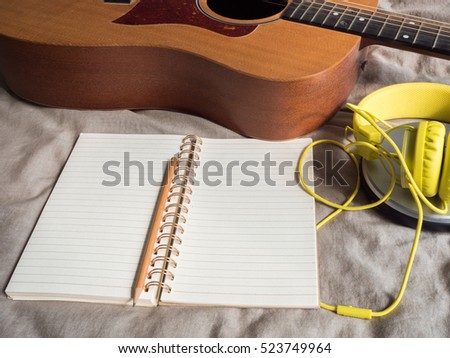 CD player,headphone,notebook,pencil and guitar on bed