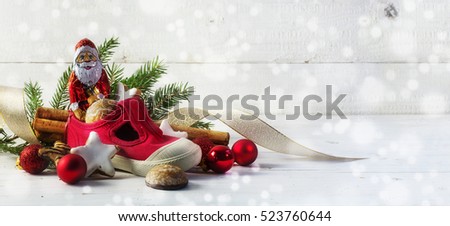 Children's red shoe filled with sweets and christmas decoration for Nicholas day on the 6th December in Germany, white wooden background with bokeh lights and copy space, panorama, selective focus