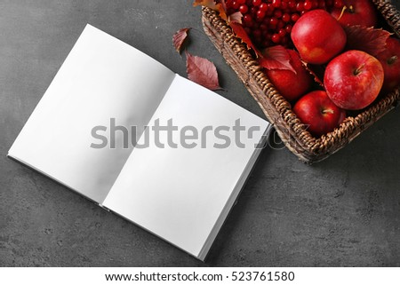 Opened book and basket with autumn apples on grey table