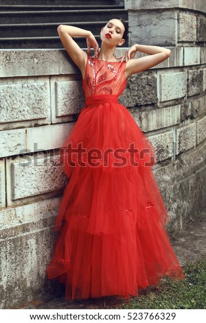 fashion outdoor photo of gorgeous young bride with dark hair in elegant red wedding dress posing beside old castle