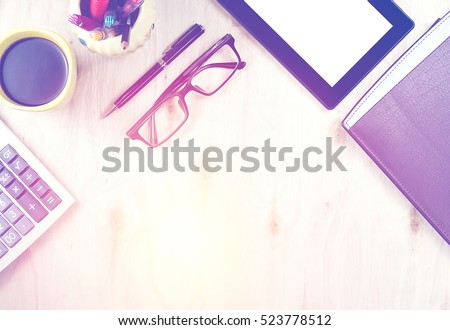 Brown glasses and tablet PC with blank screen, a cup of coffee, finance calculator,  notebook, pen and office supply on wooden background. Office table desk in top view. Vintage cool tone effect
