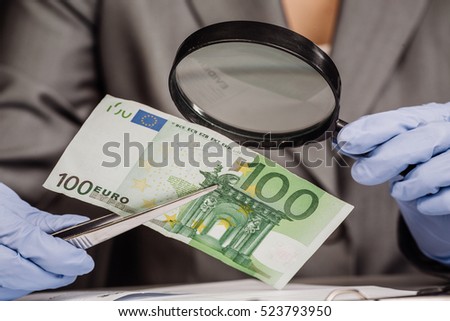Expert with magnifying glass checks suspicious money