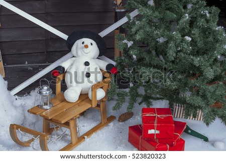 Snowman on a wooden sleigh with a Christmas tree in the background at home. Christmas.
