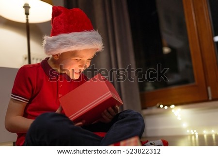 Little boy in red Santa Claus cap opening a Christmas gift