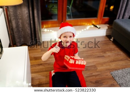 Little boy in red Santa Claus cap holding a Christmas gift