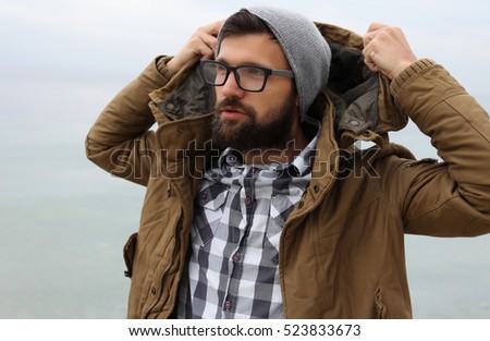 Outdoor Portrait of a handsome brutal bearded man with dark beard and mustache dressed in winter clothes,covered with frost.man in glasses,handsome man wear coat and grey hat.hipster man style
