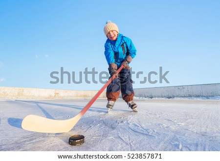 Winter games. Young happy child playing ice hockey on an outdoor ice rink. Focus on the boy.