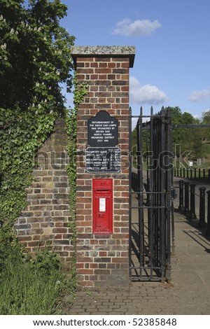 Ham Gate to Richmond Park in Kingston upon Thames. The brick pillar has a red Post box and several signs