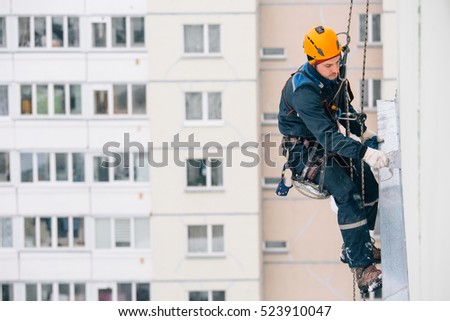 Industrial climber in helmet and uniform puttying wall on height. Risky job. Extreme work. Worker alpinist. Royalty-Free Stock Photo #523910047