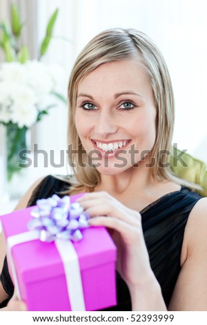 Glowing woman opening a gift sitting on a sofa at home