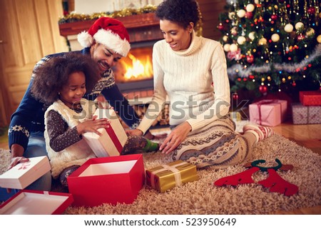 Happy family in Christmas morning opening present in home front of Christmas tree
