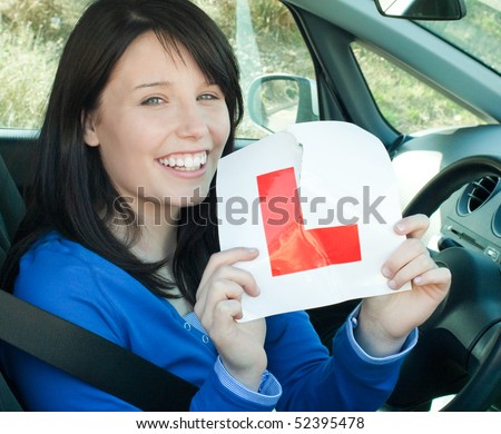 Happy teen girl sitting in her car tearing a L-sign after having her driver's licence