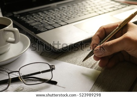 Selective focus table : Businessman use pen with eyeglass, mobile phone,laptop, note book on the wooden table.working Business concept with effect light added