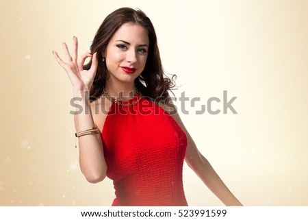 Pretty young girl making OK sign on ocher background