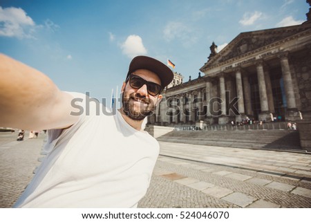 Happy bearded guy taking selfie near Reichstag in Berlin. Funny hipster student taking picture for travel blog in Germany.