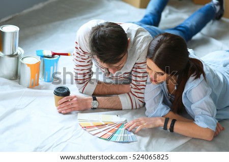 Couple choosing paint colour from swatch for new home lying on wooden floor Royalty-Free Stock Photo #524065825