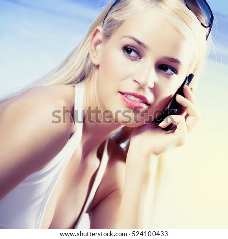 Portrait of happy smiling young beautiful woman with cell phone on beach