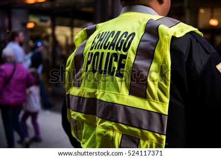 The back of a Chicago police officer controlling the crowd at a rally downtown in Chicago, IL wearing a yellow reflective vest on a sunny day by the tracks in the Loop.