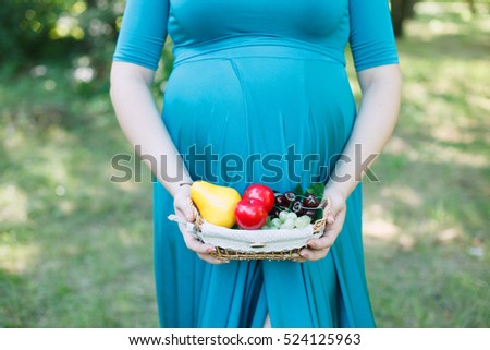 belly of pregnant woman with fruit basket on greenery background