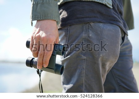 Asian male's hand holding binoculars in the field outdoor, Technology Binoculars Scope background concept 
