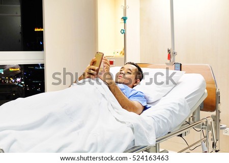 Male Patient Using Mobile Phone In Hospital Bed