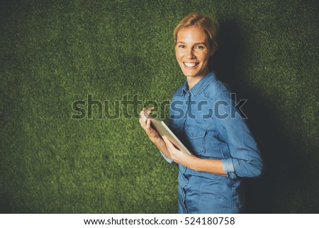 Young woman posing with tablet by green wall