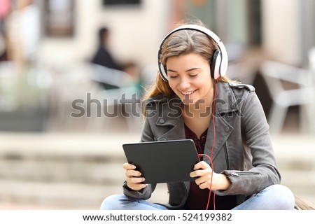 Beautiful fashion girl learning on line with a tablet and headphones sitting on a bench in the street Royalty-Free Stock Photo #524199382